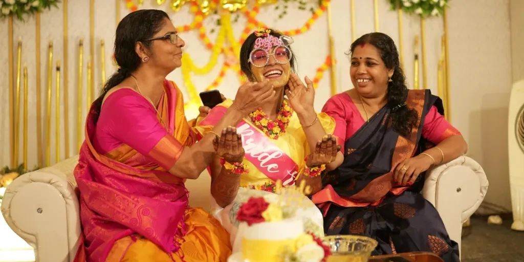 A joyous moment at an Indian Haldi ceremony with three women celebrating together indoors