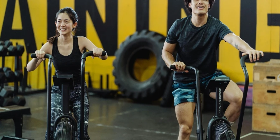 A man and woman enjoying a workout on indoor cycles at a gym, expressing fitness and joy