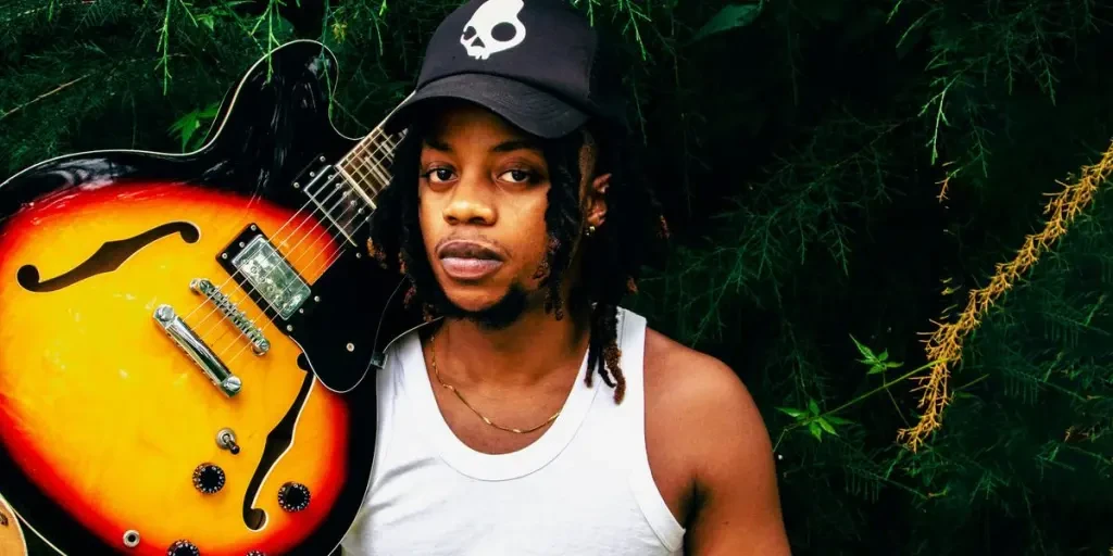 A man holding a guitar in front of a tree