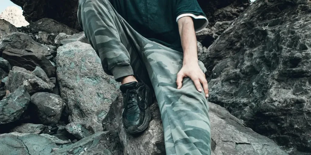 A man in casual attire poses thoughtfully on a rocky mountain with a moody sky