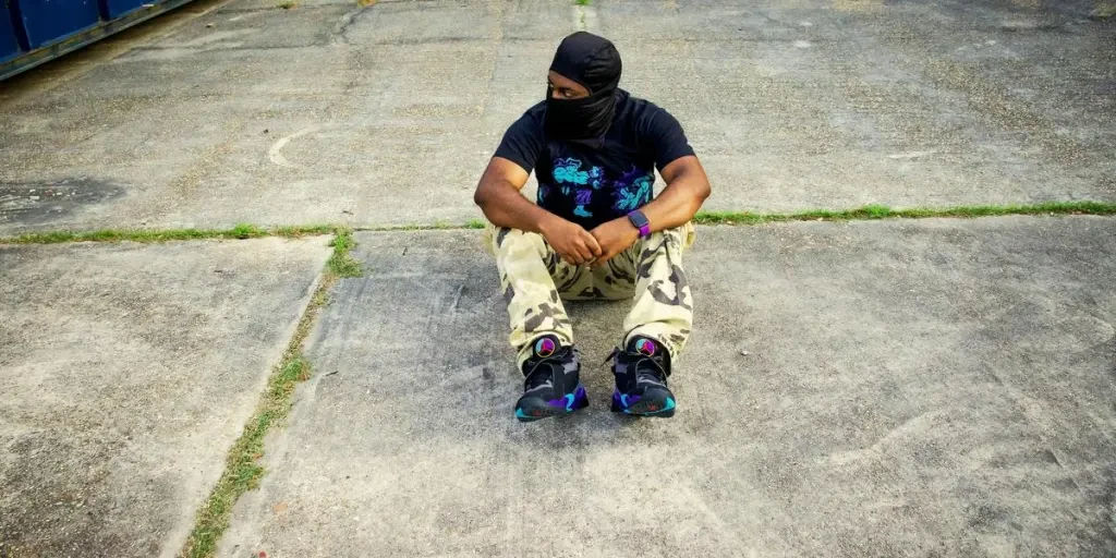 A man in urban fashion poses on concrete, wearing sneakers and camo pants