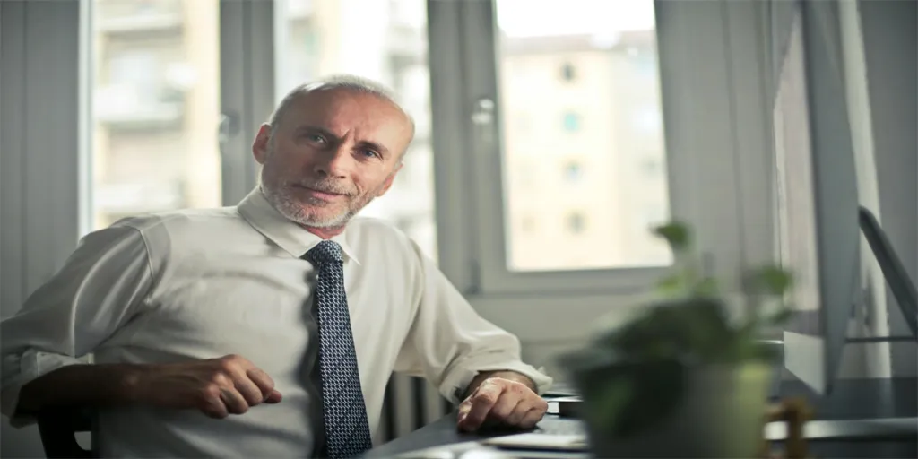 A mature man in professional attire smiling in an office setting by Andrea Piacquadio