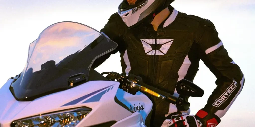 A motorcyclist on a white Kawasaki Ninja bike pauses at sunset, showcasing sleek design and riding gear