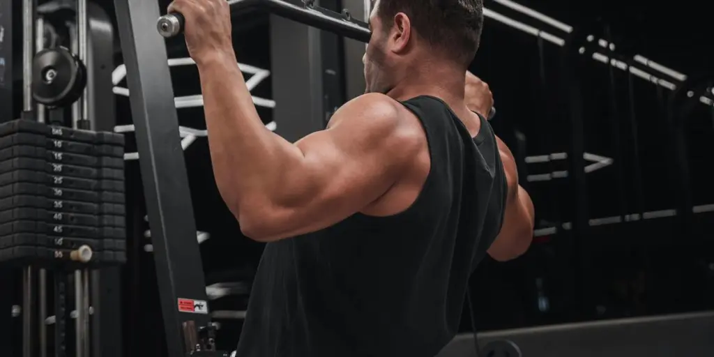 A muscular man performs a lat pulldown exercise on gym equipment, showcasing strength