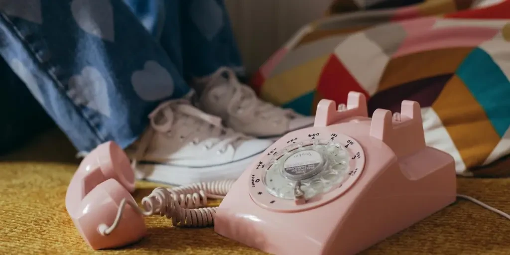 A nostalgic pink rotary telephone on a vintage carpet with jeans featuring heart patches