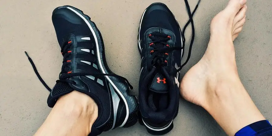 A pair of black sneakers next to bare feet on a gray surface