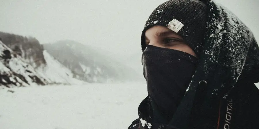 A person dressed for winter, standing in a snowy mountainous landscape, conveying a sense of adventure