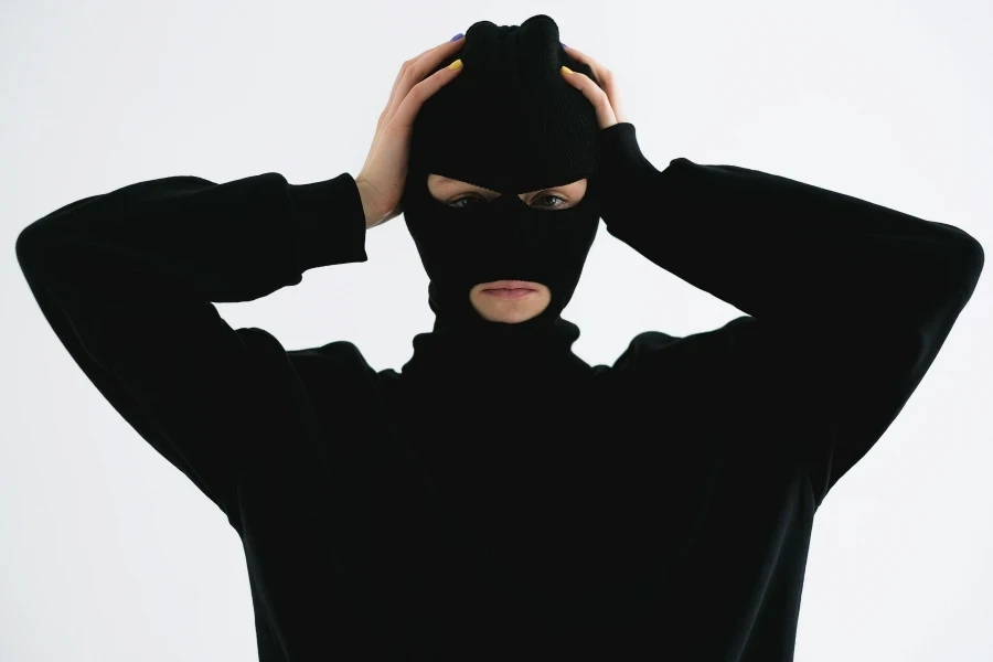 A person in a black balaclava with hands on head creates a mysterious and suspenseful vibe