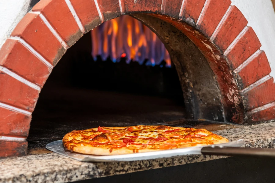 A person removing a baked pizza from an oven