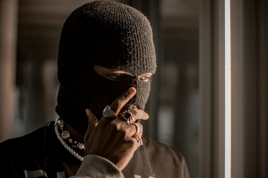 A person wearing a black balaclava adorned with rings and necklaces, creating an air of mystery