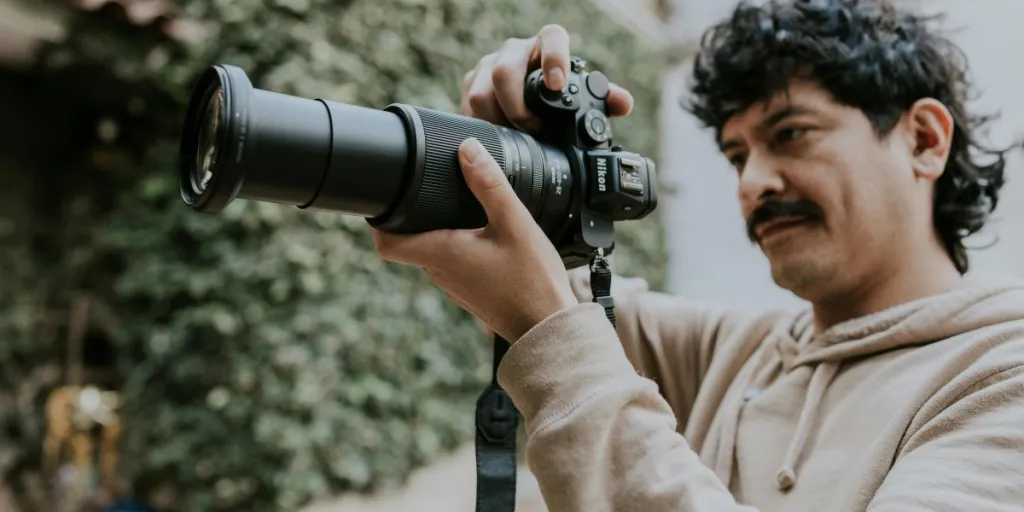 A photographer adjusts settings on a Nikon camera with a telephoto lens outdoors