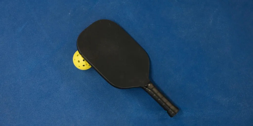 A pickleball paddle and ball on a textured blue surface, showcasing sports equipment