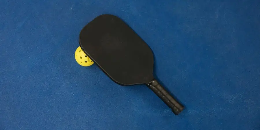 A pickleball paddle and ball on a textured blue surface, showcasing sports equipment