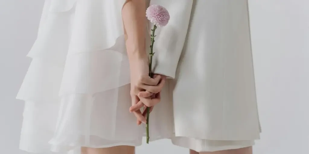 A romantic scene with a couple in white holding a single pink flower, symbolizing love and elegance