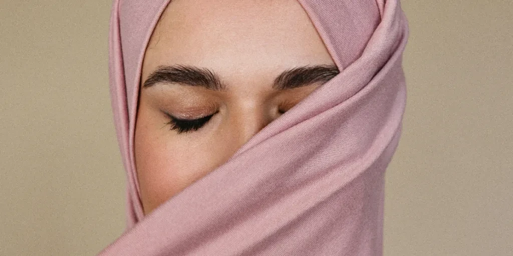 A serene close-up of a woman with closed eyes wearing a pink hijab