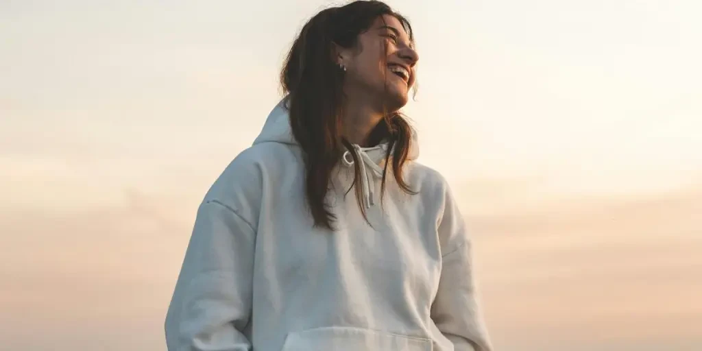 A smiling woman in casual clothing enjoys a sunset walk on a tranquil beach