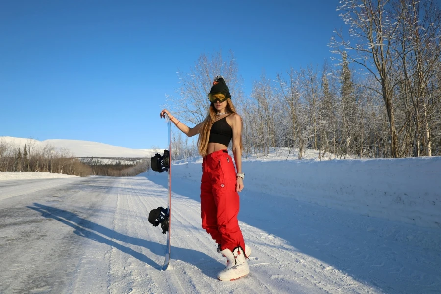 A snowboarder in vibrant red gear poses on a snowy road in sunny winter conditions in Kirovsk, Russia