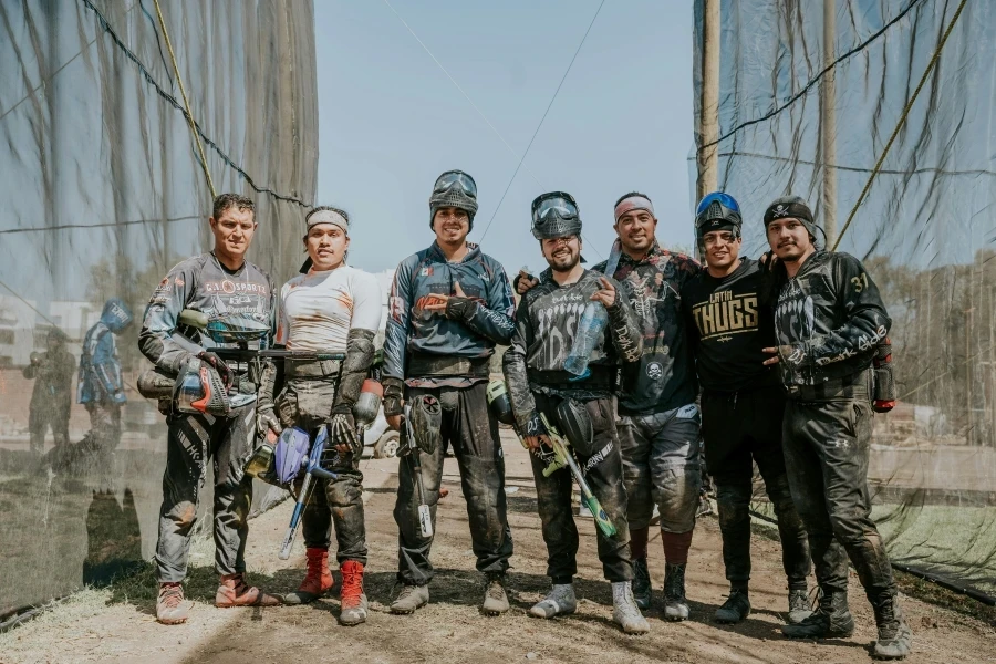 A team of men in paintball gear posing outdoors with smiles and paint markers