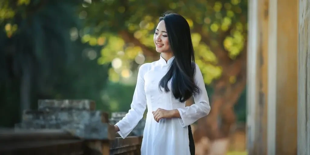 A woman dressed in a white garment stands barefoot on dry, sandy grass, creating a whimsical outdoor scene