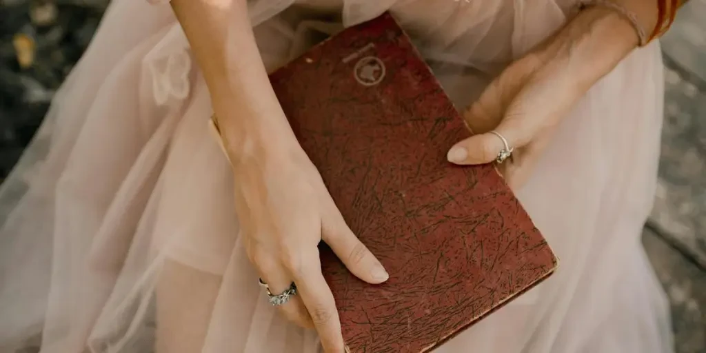 A woman gracefully poses with an old book, wearing a flowing tulle dress, creating a timeless fashion scene