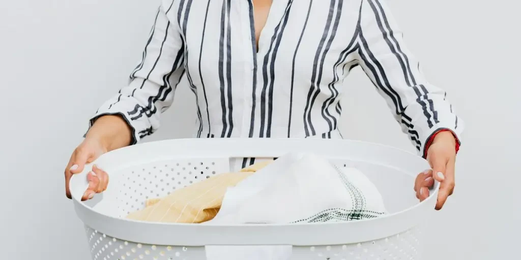 A woman holding a laundry basket filled with clothes against a plain white background by Photo