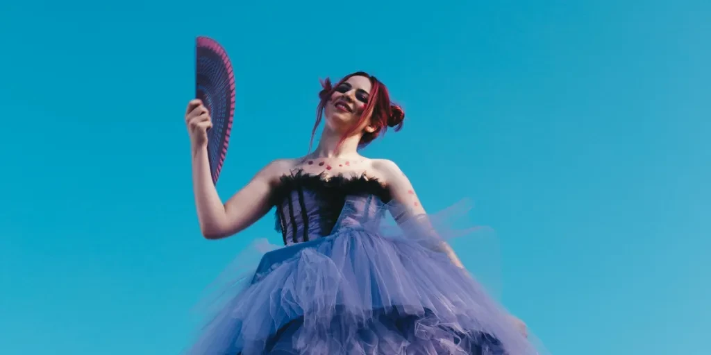 A woman in a purple dress holding a fan, set against a bright blue sky, showcasing elegance and fashion 