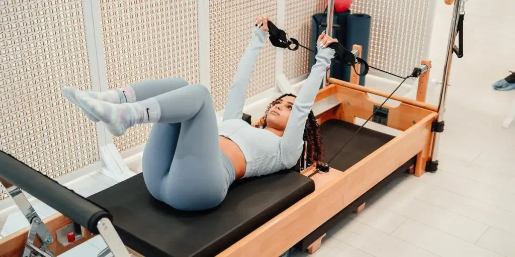 A woman performs pilates exercises on a reformer machine indoors, focusing on fitness and flexibility