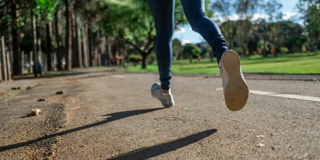 A woman running outdoors on a sunny day along a scenic park trail, focusing on fitness and health