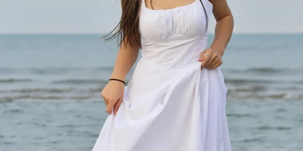 A woman stands gracefully in a white dress by the sea, embodying elegance and tranquility