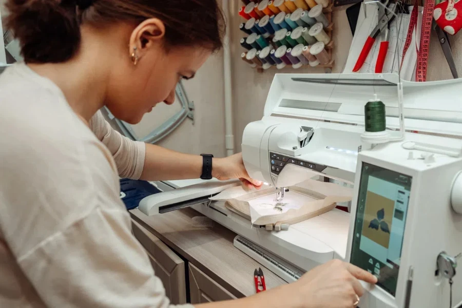 A woman tailor makes embroidery on an embroidery machine in a home workshop