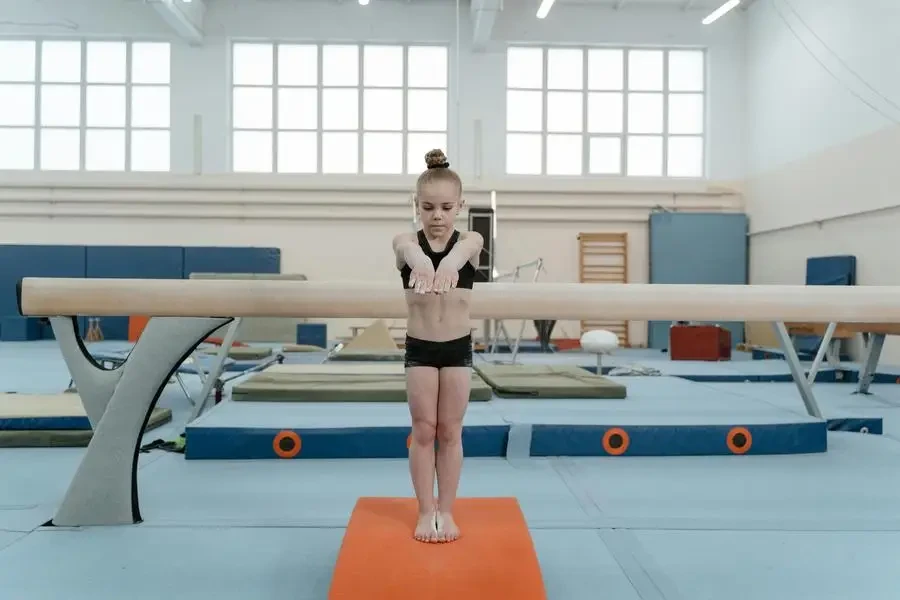 A young girl focuses while performing a balance beam routine in a gym. Gymnastics and training setting