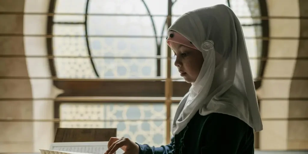 A young girl in a hijab reads the Quran, immersing herself in Islamic culture and tradition indoors