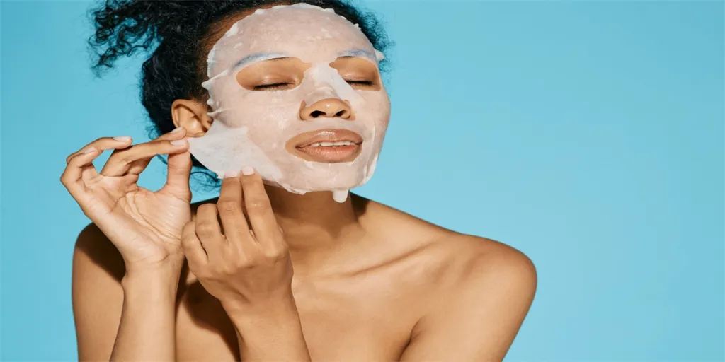 African American woman applies cosmetic tissue facial mask for hydrating and moisturizing and glowing face skin