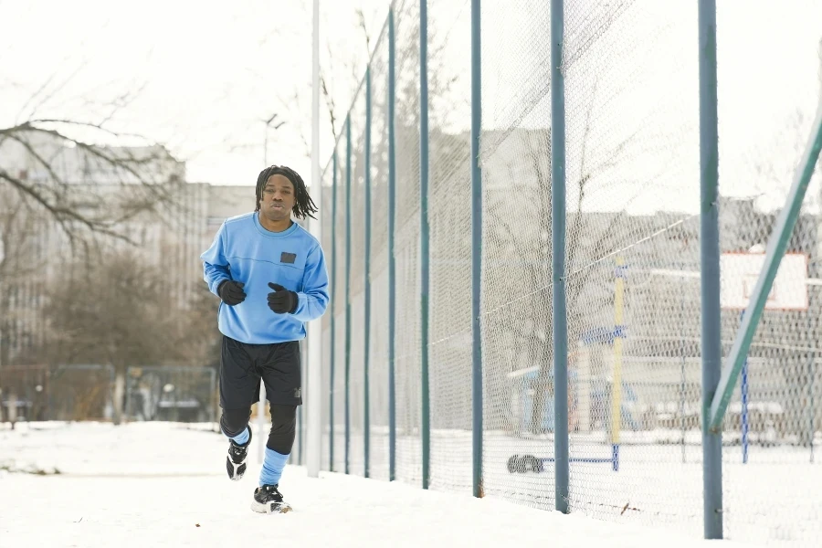 An adult man jogging on a snowy path beside a fence, embracing a healthy lifestyle in winter