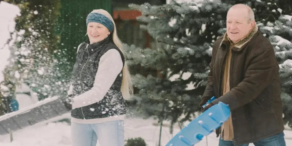 An elderly couple happily shovels snow together outdoors, embracing the winter season