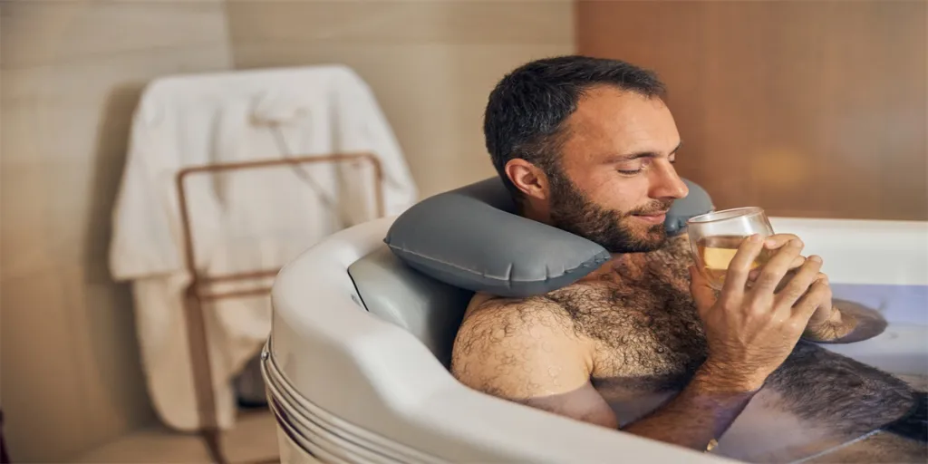 Bearded gentleman enjoying delicious drink while relaxing in bathtub