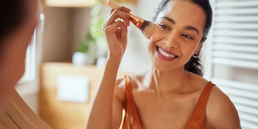 Beautiful girl applying makeup using powder brush before going to work