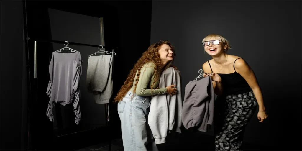 Beautiful smiling young woman stylist designer helping choose clothes to customer client at fashion boutique