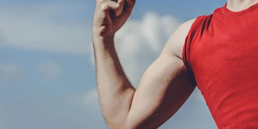 Close-up of a flexed arm in a red shirt against a clear blue sky, symbolizing strength and empowerment