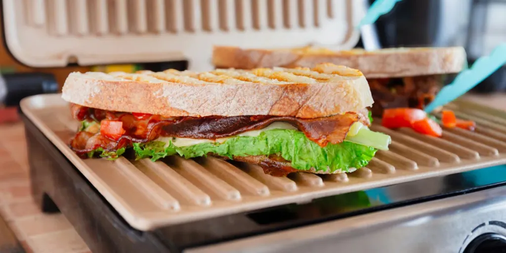 Close-up of a grilled Italian sandwich with bacon, lettuce, and tomato on a panini press, ready to be served