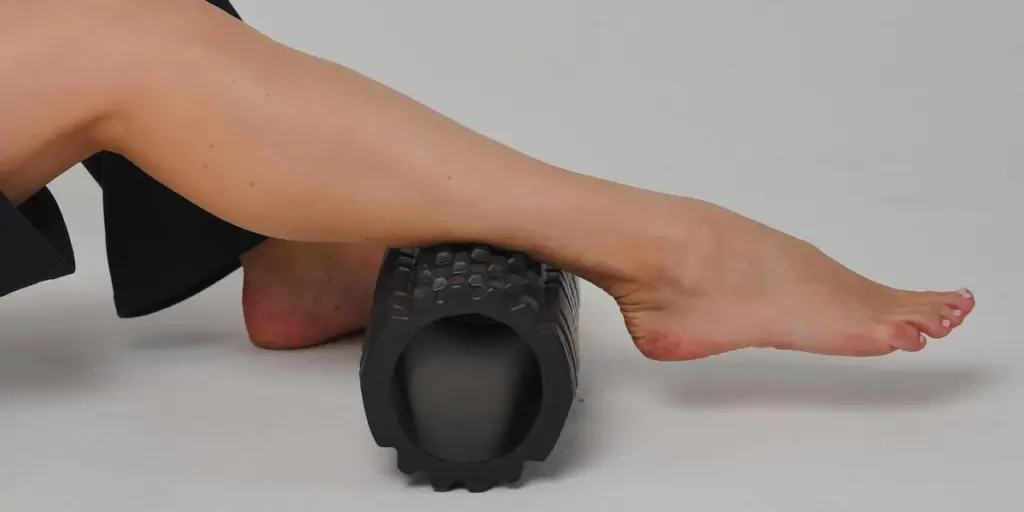 Close-up of a leg using a foam roller for stretching and muscle relief in a studio setting