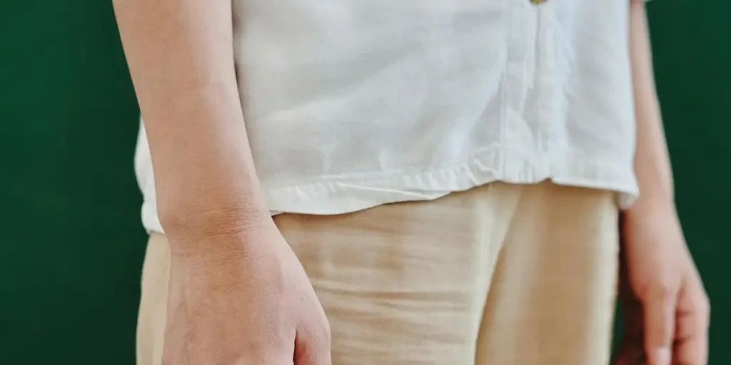 Close-up of a person in a minimalist white shirt and khaki pants against a green backdrop