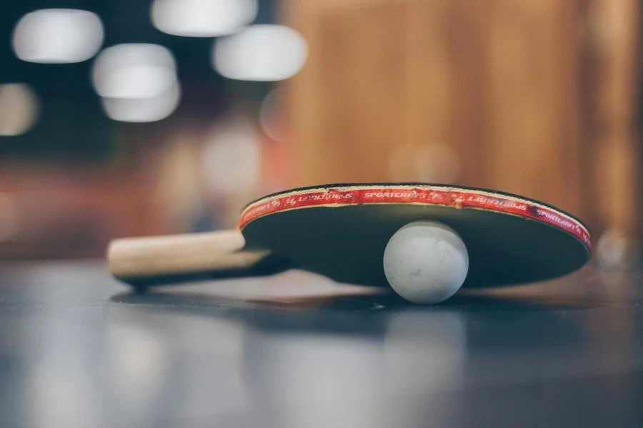 Close-up of a ping pong paddle and ball on a table with an artistic bokeh background, indoors