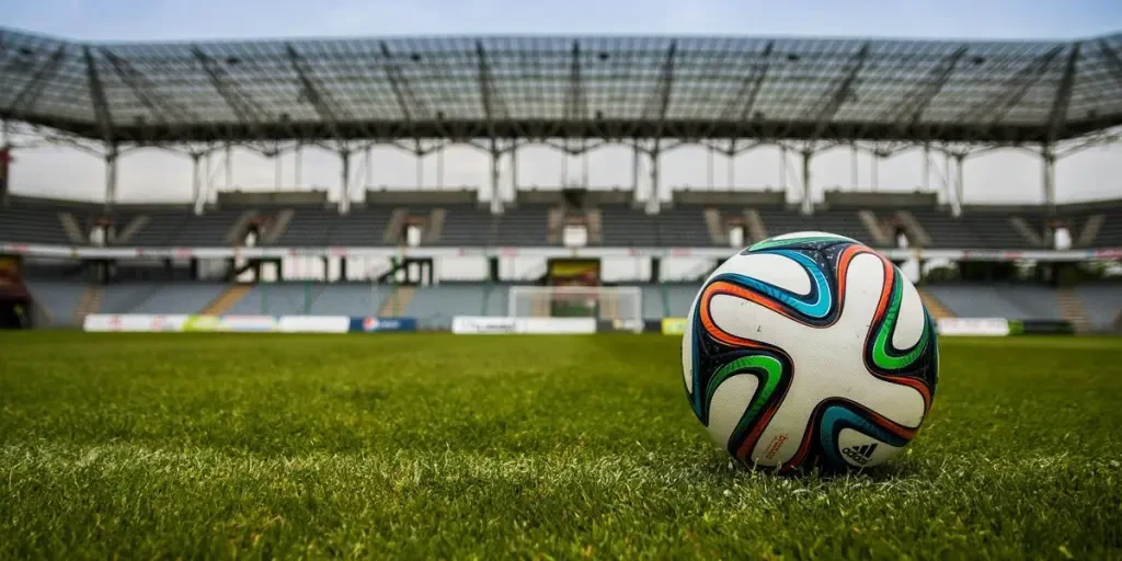 Close-up of a soccer ball on a lush grass field with an empty stadium in the background