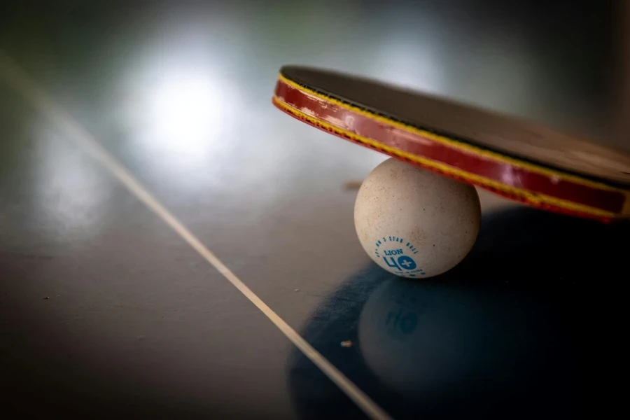 Close-up of a table tennis racket balancing on a ball indoors, emphasizing balance and sport