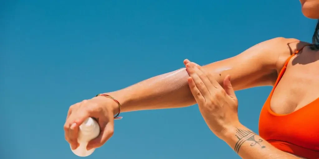 Close-up of a woman applying sunscreen on her arm under a clear blue sky at the beach