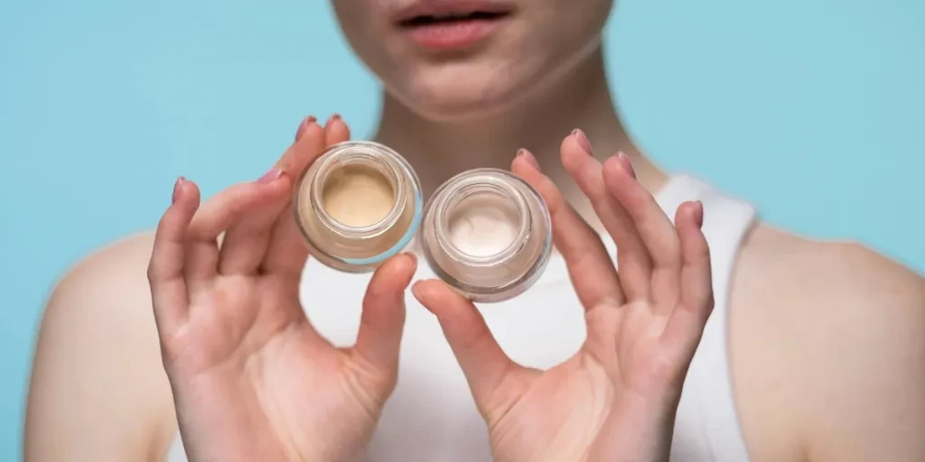 Close-up of a woman holding skincare jars against a blue background, showcasing beauty and self-care