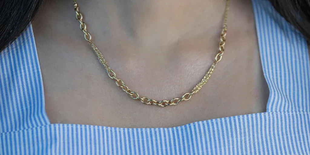 Close-up of a woman wearing a delicate gold necklace with a striped top by Maryam