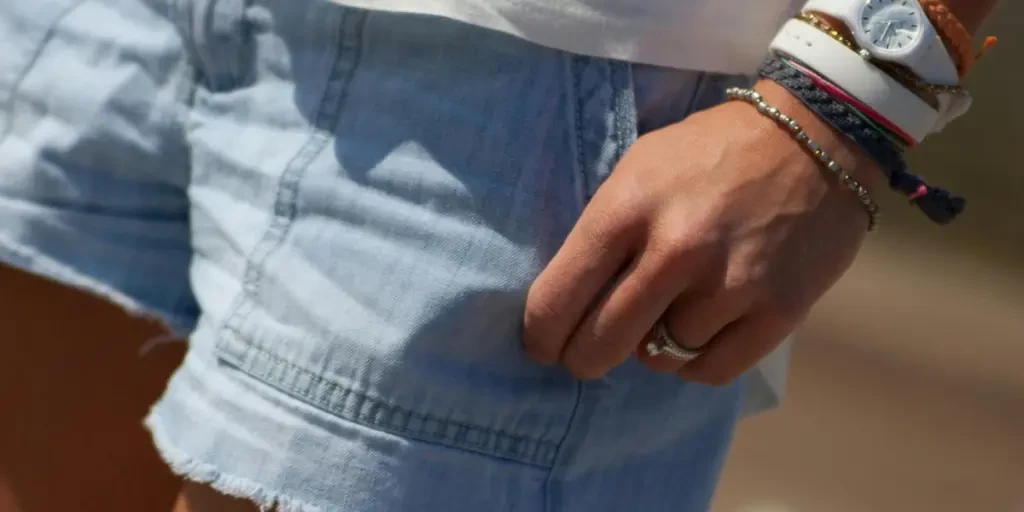 Close-up of a womans hand with bracelets and watch, wearing denim shorts