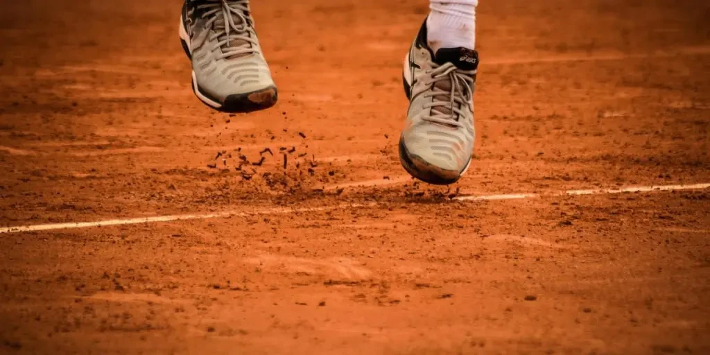 Close-up of an athletes shoes mid-jump on a clay tennis court